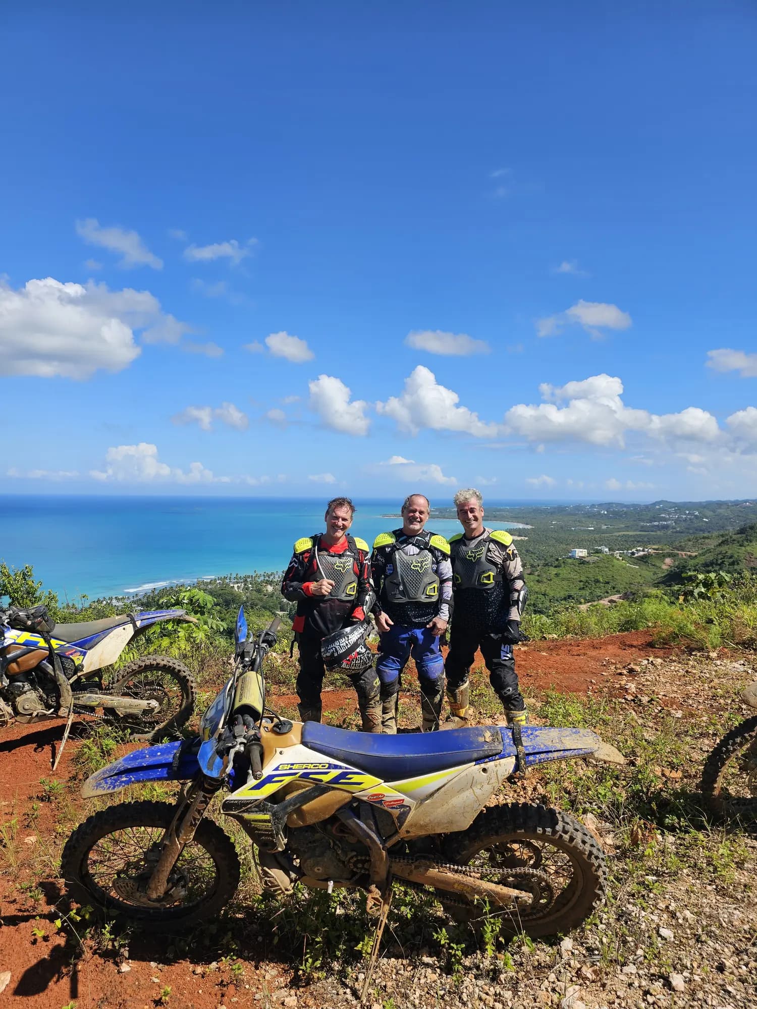 Riders and Sherco bikes on a coastal hill