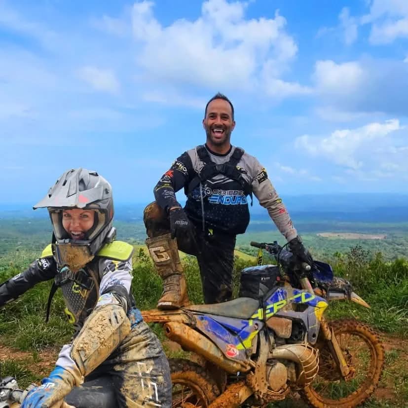 Patrick Poirier and Élodie Bergeron, muddy and smiling on a hilltop with their enduro bikes