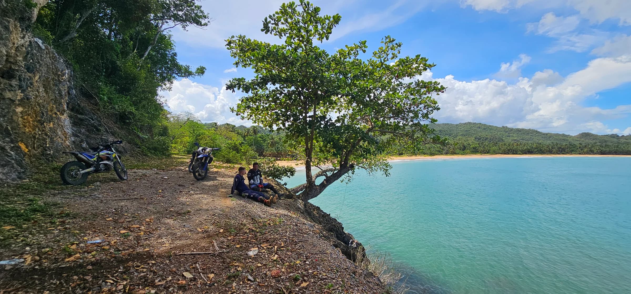 Turquoise cove with a lone tree, riders resting and bikes parked on the shore