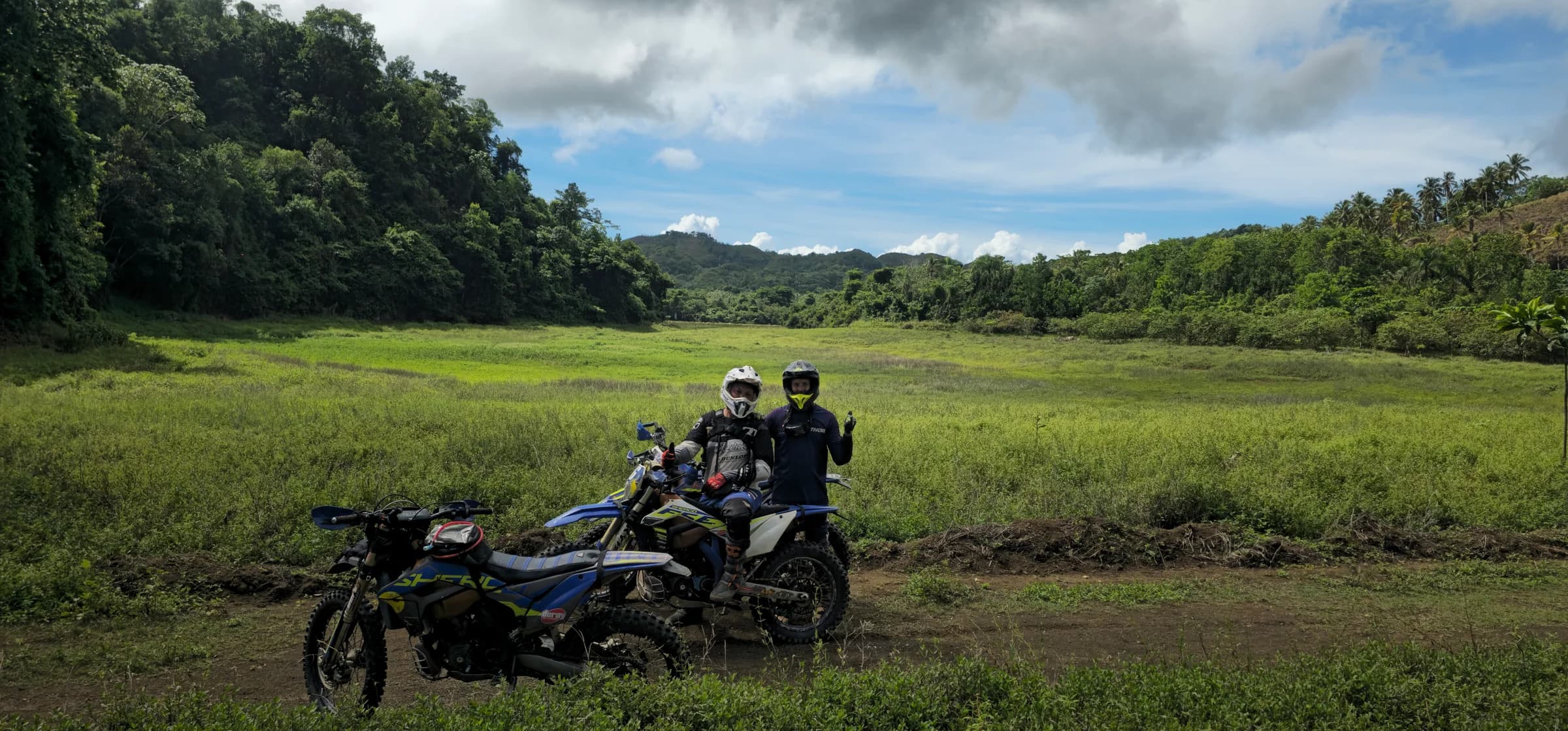 Two riders and their bikes parked in a green valley under a big sky